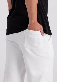 Witte katoenen broek met een gladde textuur en zijzakken, gecombineerd met een zwart shirt met korte mouwen, dat een ontspannen pasvorm heeft.