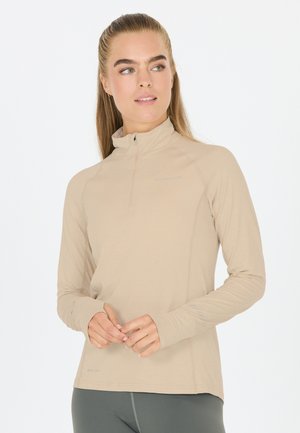 Top beige chiaro con zip e maniche lunghe, dotato di un colletto alto e fori per il pollice. Realizzato in tessuto ad asciugatura rapida, con una trama liscia e dettagli di branding discreti.