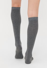 Calze grigie al ginocchio con texture a costine e dettaglio a contrasto sul risvolto. Realizzate in materiale morbido, progettate per offrire comfort e copertura.