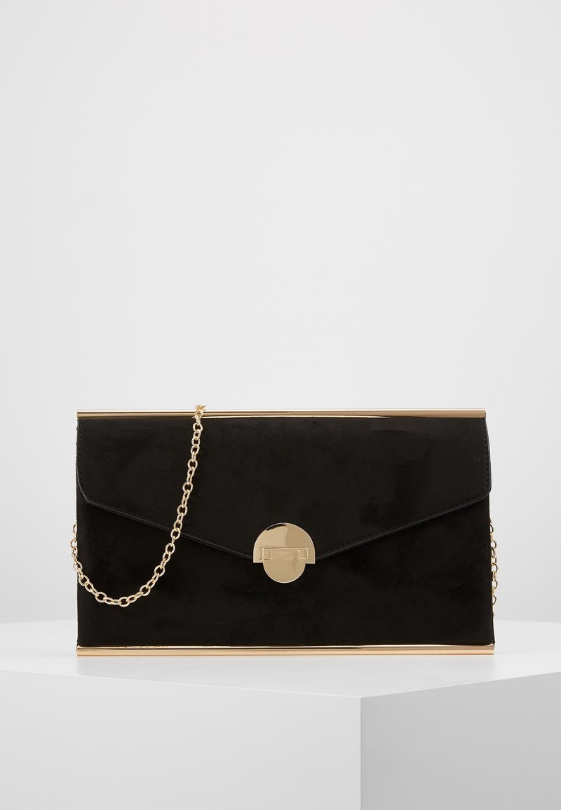 Pochette rectangulaire noire avec bordure dorée, fermoir rond en or et fine bandoulière chaîne dorée sur une surface blanche.