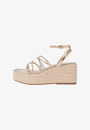Sandali wedge metallici oro con una piattaforma in juta intrecciata, caratterizzati da più cinturini sottili e una fibbia alla caviglia per un supporto maggiore.