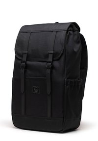 Zaino nero con un design strutturato, materiale in tessuto, spallacci regolabili, tasca frontale e una patta pieghevole fissata da fibbie.