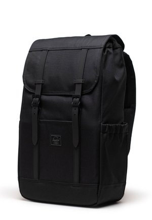 Sac à dos noir au design structuré, en matériau textile, avec des bretelles ajustables, une poche avant et un rabat replié sécurisé par des boucles.