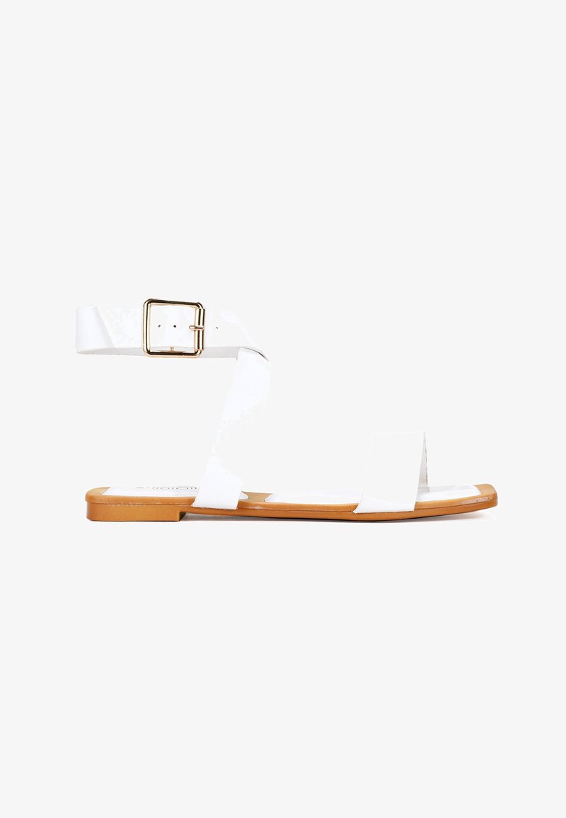 Sandalias planas blancas con dos cintas anchas y cierre de hebilla. La suela es color marrón claro, con un acabado suave y elementos de diseño mínimos.