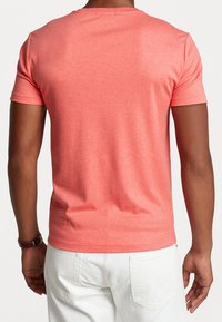 Koraliowy t-shirt z krótkim rękawem, wykonany z miękkiej tkaniny, z okrągłym dekoltem i luźnym krojem. Widoczne szwy na dole i rękawach.