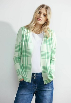 Cardigan à carreaux vert clair avec une texture douce, design à l'avant ouvert, manches longues, porté sur une chemise blanche et assorti avec un jean bleu.