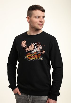 Sort sweatshirt med grafik af en karakter fra "Street Fighter", der viser en knyttet næve og røde accenter i designet.