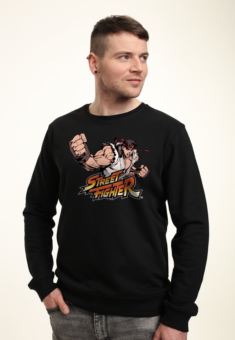 Felpa nera con una grafica di un personaggio di "Street Fighter," che mostra un pugno chiuso e accenti rossi nel design.