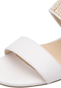 Sandale en simili cuir blanc avec une large sangle et un accent en textile tissé sur le dessus. Semelle de couleur neutre et design minimaliste.