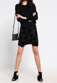 Black geometric-patterned skirt with a textured surface, paired with a fitted black long-sleeve top and black open-toe heeled booties.