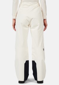 Pantaloni da sci bianchi con un design a gamba larga, caratterizzati da un pannello inferiore nero e un dettaglio del logo sul lato destro. Tessuto liscio e impermeabile.