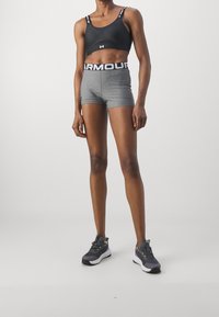 Reggiseno sportivo nero con dettagli del logo, pantaloni corti grigi attillati con vita alta e scarpe da ginnastica grigie con accenti colorati.