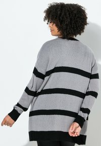 Pitkähihainen, ylisuuri neuletakki vaaleanharmaana, jossa on mustia vaakaraitoja. Neulepinta, löysä malli ja resorit hihansuissa.