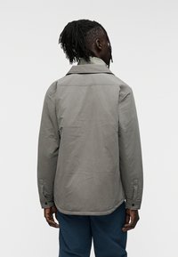 Γκρι ελαφρύ μπουφάν με δομημένο γιακά, μανσέτες με κουμπιά και λεία υφή, σχεδιασμένο με κανονική εφαρμογή και διακριτικό ματ φινίρισμα.