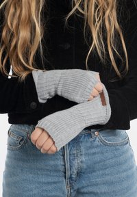 Guanti senza dita grigi lavorati a maglia con texture a coste, indossati sopra una giacca in corduroy nera, con un dettaglio in pelle discreto.