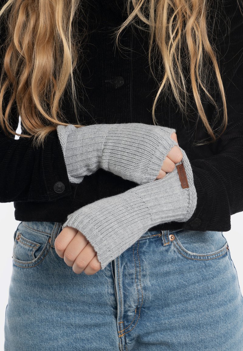 Guanti senza dita grigi lavorati a maglia con texture a coste, indossati sopra una giacca in corduroy nera, con un dettaglio in pelle discreto.