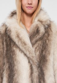 Abrigo de pelo sintético en tonos degradados de crema y gris, con un gran collar y una superficie suave y texturizada, que proporciona una apariencia lujosa.