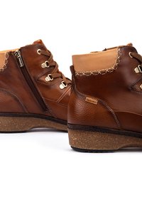 Bottes de cheville en cuir marron avec fermeture à lacets et à zip, présentant un dessus contrastant en tan, une finition texturée et une semelle semblable au liège.