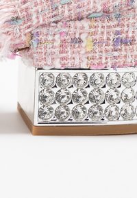 Rosa tweedtyg med färgglada trådar ovanpå en silvermetallisk bas, prydd med runda rhinestones i ett rutmönster. Rundad beige botten.