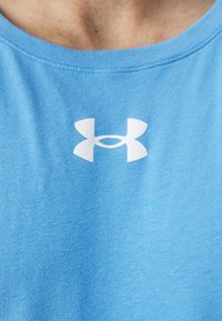 Maglietta in cotone azzurro chiaro con scollatura rotonda, caratterizzata da un logo bianco di Under Armour nella zona del petto. Texture liscia, design casual.