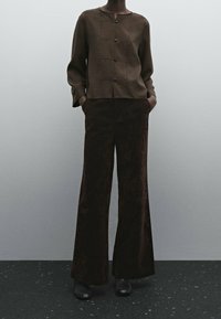 Haut marron à manches courtes avec fermeture par boutons et tissu texturé, associé à un pantalon marron à jambes larges. Les deux pièces ont une coupe décontractée.