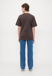 Hnědé oversized tričko s krátkými rukávy, bavlněný materiál, doplněné o světle modré rovné džíny a bílé tenisky s multicolor akcenty.