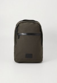 Mochila de tela verde oscuro con forma rectangular, con una banda negra horizontal en la parte frontal y un parche de logo en la parte inferior.