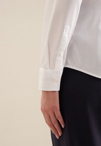 Witte button-up shirt met een puntige manchet, gemaakt van gladde stof, met twee knopen in een contrasterende kleur op de manchet.