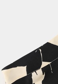 Gros plan d'un tissu plié avec des formes abstraites noires et beiges sur une surface textile lisse.