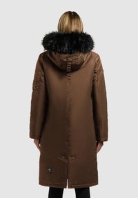Brun polstret parka med en sort faux fur hætte, en lynlås og knaplukning, samt sidelommer, der har et logo-accent nær kanten.