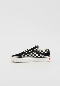 Basket basse à motif à carreaux noir et blanc avec des lacets blancs et une semelle épaisse en caoutchouc blanc sur un fond clair uni.
