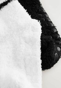 Schwarz-weißer Plüschstoff mit einer strukturierten Oberfläche und kreisförmigen Gummiakzenten auf beiden Seiten. Weiche, flauschige Textur.