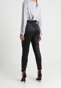 Svarta högmidjade byxor med en slät textur, med en figursydd siluett och dragkedjor vid vristerna, tillsammans med en ljusgrå blus.