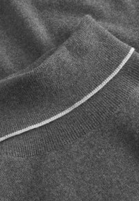 Maglione grigio con una texture morbida, caratterizzato da un colletto a coste e una striscia bianca all'altezza del collo. Design semplice con una finitura liscia.