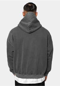 Grå hættetrøje med en rummelig hætte, ribbede manchetter og kant. Stoffet virker blødt og struktureret med faldne skuldre for en afslappet pasform.