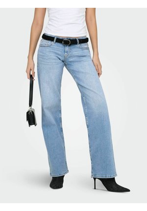 Žena v svetlomodrých džínsach s rovnými nohavicami, čiernym pleteným opaskom, čiernymi špicatými čižmami na vysokom opätku a s malou čiernou kabelkou v ruke.