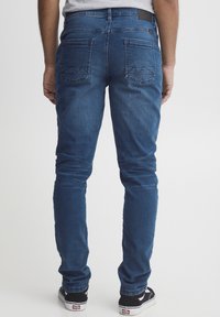Jeans din denim albastru, slim-fit, cu o textură netedă, ușor decolorate, și două buzunare pe spate cu accente de cusături zigzag.