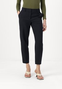 Pantalons ajustés bleu marine, avec une texture lisse et des poches latérales, associés à des sandales à talons crème.