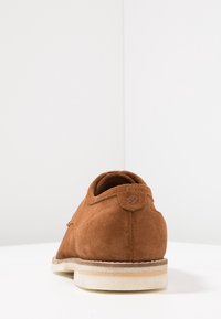 Chaussure en daim marron à silhouette arrondie, surface texturée et semelle en caoutchouc légère et superposée. Dotée d'un petit détail en cuir au talon.