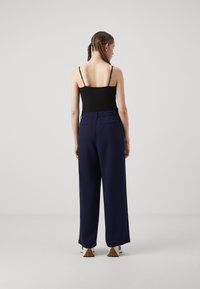 Navy wide-leg trousers with a relaxed fit, featuring an elastic waistband and back pockets. Paired with a black spaghetti strap top.