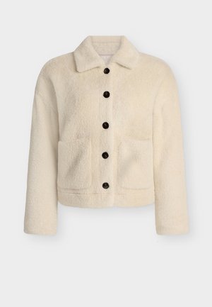 Fleece bunda v krémové barvě s límcem, zapínáním na knoflíky vpředu a dvěma našitými kapsami. Vybavena černými knoflíky a strukturovaným, jemným povrchem.