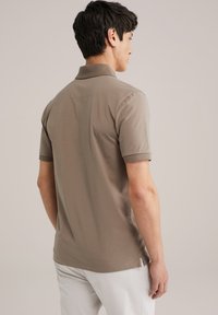 Kastanjebruine polo met korte mouwen, een kraag en een rechte zoom. Gemaakt van een gladde stof met zijsplitten voor bewegingsgemak.