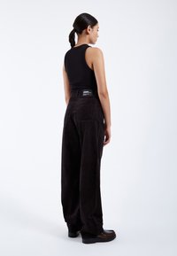 Pantalones de pana anchos en color negro con cintura alta y bolsillos traseros, combinados con una camiseta ajustada negra; textura suave y minimalismo en la marca.