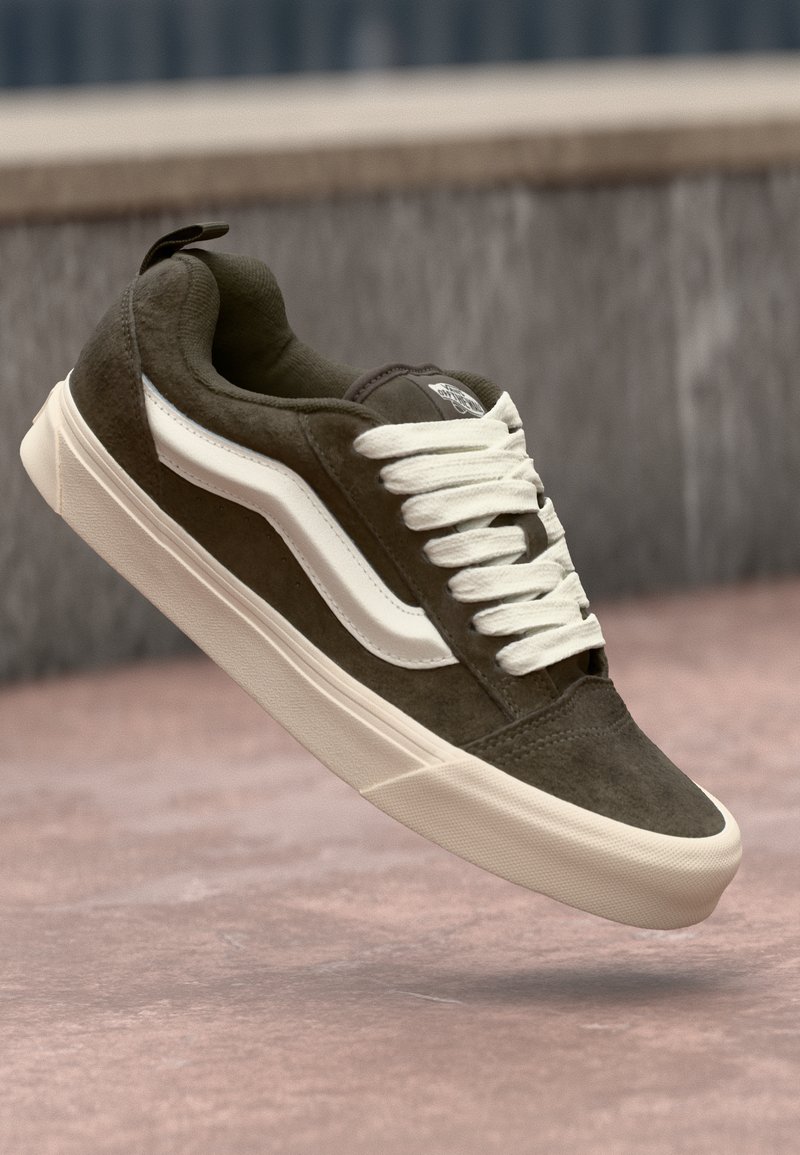 Dark green suede sneaker with white laces and a contrasting white side stripe. Features a textured upper and a slightly raised rubber sole.