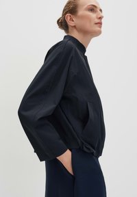 Navy blue lightweight jacket with a high collar, side pockets, and relaxed fit. Features smooth texture and contrasting seam detailing.