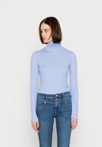 Top azul claro de manga longa com gola alta e textura canelada, combinado com jeans azuis ajustados com um design clássico de cinco bolsos.