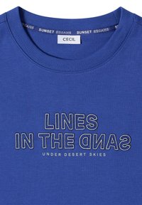 T-shirt bleu col rond avec les textes "LINES IN THE SAND" et "UNDER DESERT SKIES" brodés en fil contrastant sur le devant.