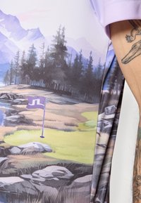 Košeľa s krátkym rukávom so scénickým potlačou krajiny v jemných odtieňoch, zobrazujúcim hory, stromy a golfový znak na zelenom pozadí.