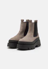 Botas tobilleras de ante gris con paneles elásticos laterales negros, suela de goma negra gruesa, punta redondeada y lengüetas para facilitar su puesta.