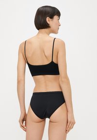 Černá sada spodního prádla sestávající z žebrované podprsenky s nastavitelnými ramínky a vroubkovanými okraji, doplněná o kalhotky s vysokým pasem. Měkký materiál, hladká textura.
